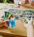 Op de foto is een gezellig moment tijdens een bordspel vastgelegd, waarbij twee mensen geconcentreerd kaarten en speelstenen vasthouden en zich onderdompelen in het boeiende spel aan een houten tafel vol strategische elementen.